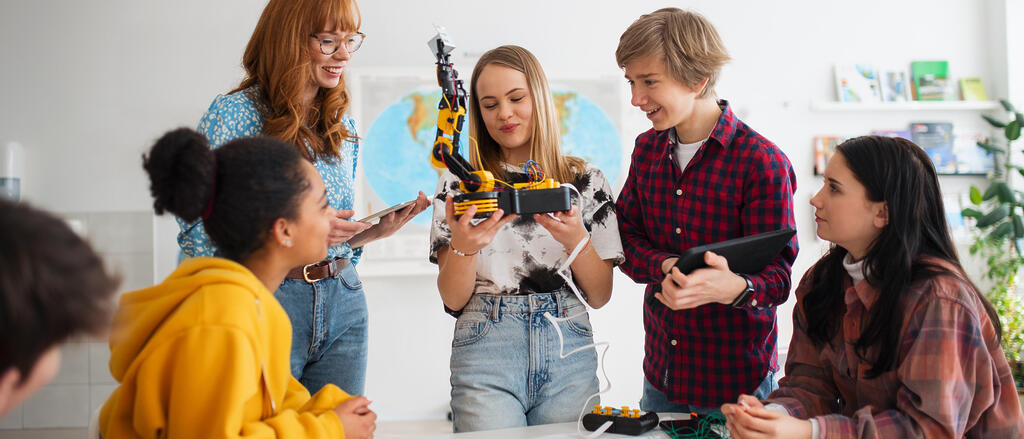 Eine Schülergruppe und ihre Lehrerin untersuchen einen Roboter